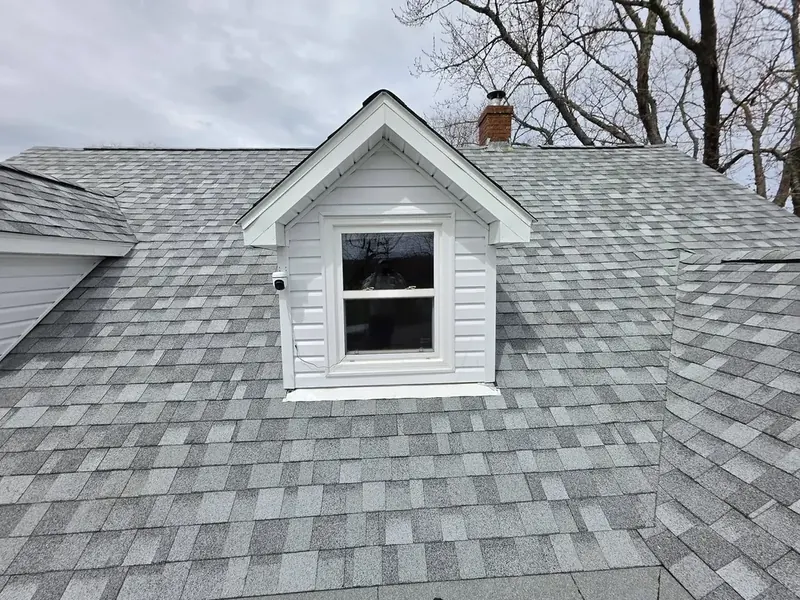 Newly shingled dormer with white trim on a steep grey roof.