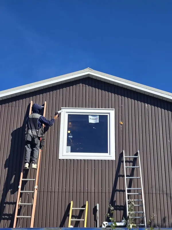 Worker installing a new window on a metal-sided home gable.